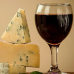 Three cheeses stacked on top of each other next to a glass of red wine
